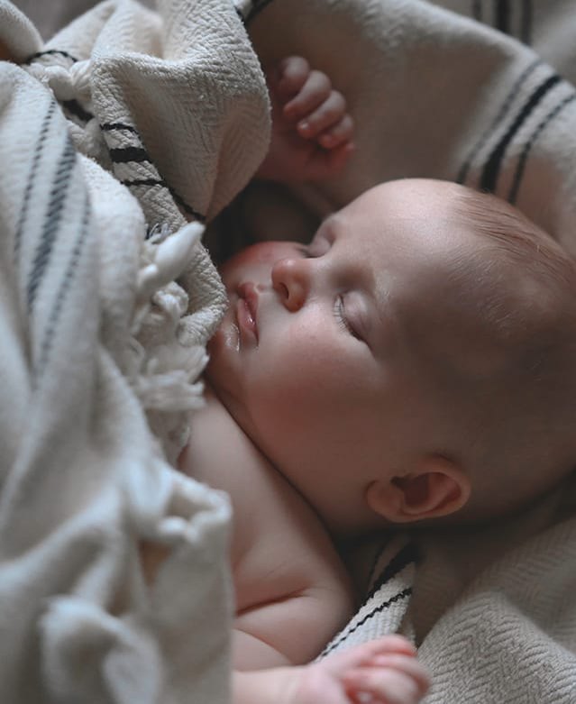 Newborn baby asleep in a cream knit blanket